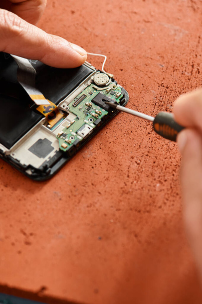 обрезанный вид профессионального ремонтника, открывающего сломанный сотовый телефон с отверткой в мастерской - Фото, изображение