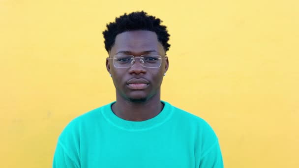 Close-up portret van jonge volwassen Afrikaanse man lachend naar camera over gele achtergrond. Vooraanzicht headshot van vrolijke zwarte man gevoel positief buiten. - Video