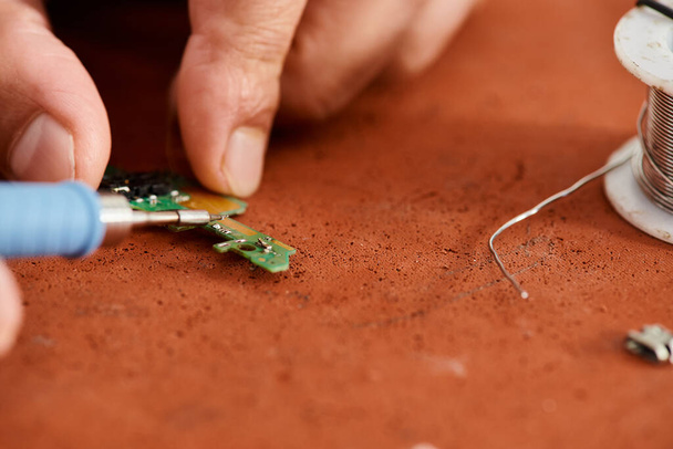 Teilansicht des erfahrenen technischen Spezialisten beim Löten elektronischer Chips in der Reparaturwerkstatt - Foto, Bild