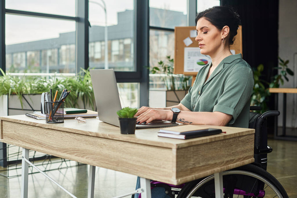 jól néz ki magabiztos nő fogyatékossággal tolószékben keményen dolgozik a laptopján az irodában - Fotó, kép