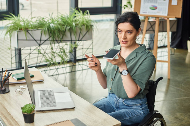 attrayant brunette femme d'affaires en fauteuil roulant enregistrement message audio en utilisant son smartphone - Photo, image