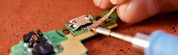 Nahaufnahme eines professionellen Reparateurs beim Löten elektronischer Chipsätze in der Werkstatt, horizontales Banner - Foto, Bild