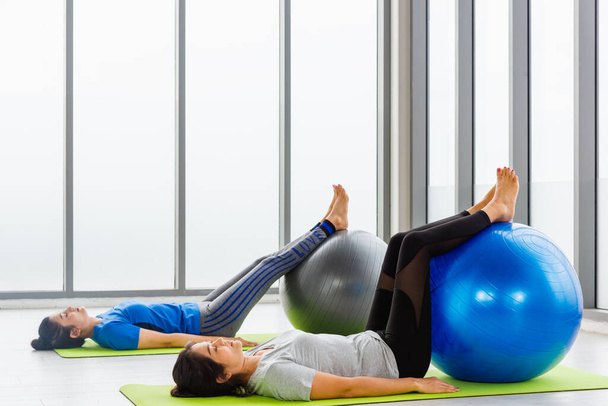 Two Asian adult and young woman in sportswear doing aerobics yoga exercise abdominal with fitness ball indoor yoga studio, fit sport healthy workout lifestyle exercise - Foto, Imagem