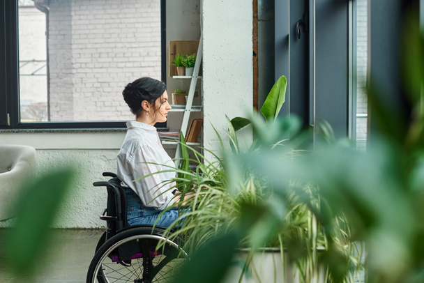 Tekerlekli sandalyede şık giyinmiş engelli bir iş kadını ofisteyken gözlerini kaçırıyor. - Fotoğraf, Görsel