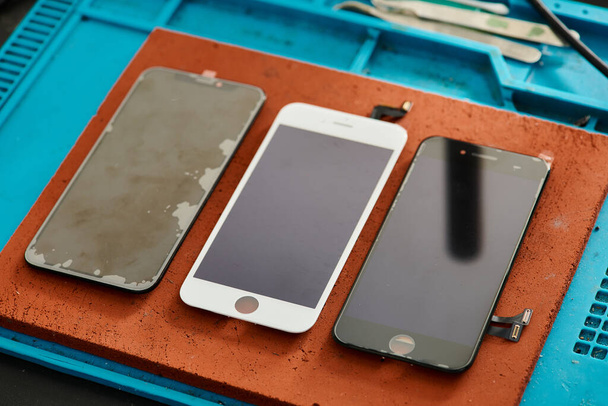 vysoký úhel pohledu na rozbité a opravené mobilní telefony na pracovním stole v dílně, opravna - Fotografie, Obrázek