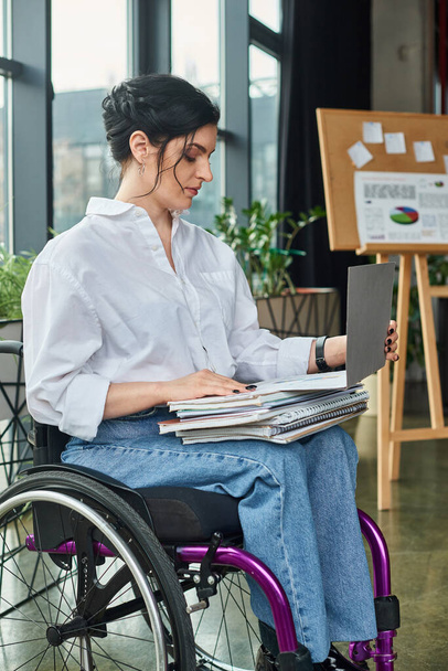 attraktive, hart arbeitende behinderte Geschäftsfrau im Rollstuhl, die mit Papierkram an ihrem Laptop arbeitet - Foto, Bild