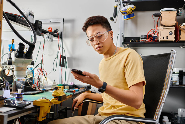 опытный азиатский работник ремонтной мастерской смотрит на смартфон во время технической диагностики - Фото, изображение