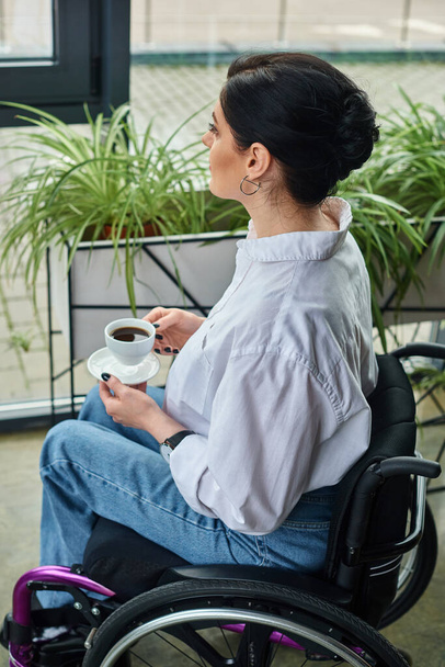 vonzó elkötelezett fogyatékkal élő nő elegáns öltözékben ül tolószékben kávéscsészével - Fotó, kép
