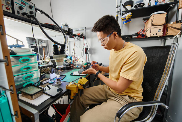profissional asiático técnico em óculos mantendo dispositivos eletrônicos no local de trabalho na oficina de reparação - Foto, Imagem