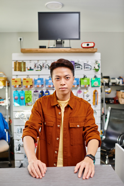 confiado asiático hombre mirando cámara en privado electrónica tienda con surtido de electrónica - Foto, imagen