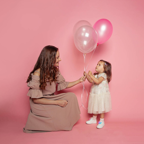Πορτρέτο της όμορφης νεαρής γυναίκας και της κόρης του κοριτσιού κρατώντας μπαλόνι σε ροζ φόντο - Φωτογραφία, εικόνα