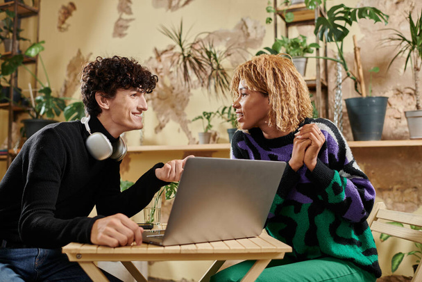 positieve Afro-Amerikaanse vrouw in beugels op zoek naar krullend vriendje in de buurt van laptop in veganistisch cafe - Foto, afbeelding