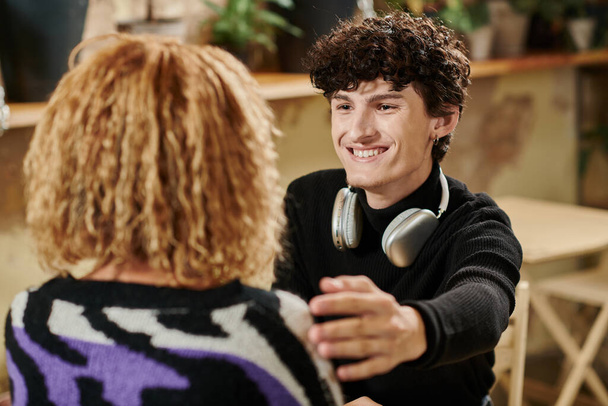curly young man with wireless headphones touching shoulder of african american girl in vegan cafe - Photo, Image