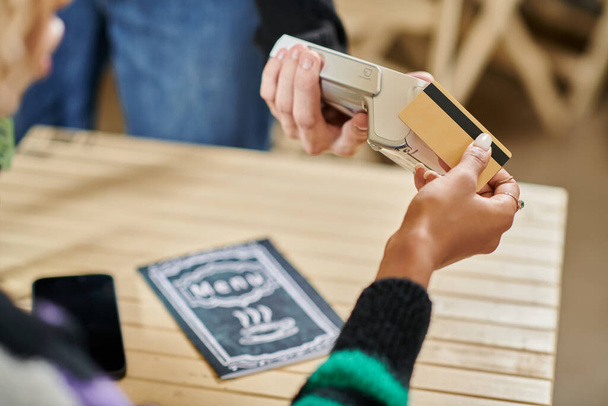 Junge Kundin hält Kreditkartenlesegerät in der Nähe, schneidet Frau beim Bezahlen in veganem Café die Hand ab - Foto, Bild