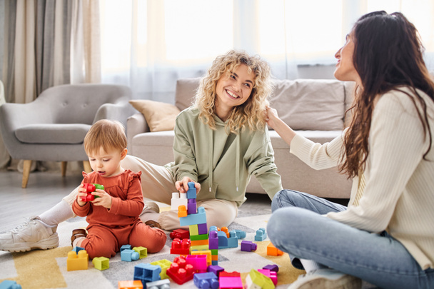 陽気で魅力的な lgbt カップルと遊ぶ赤ちゃんの女の子と遊ぶ 家でのおもちゃ, 家族の概念 - 写真・画像