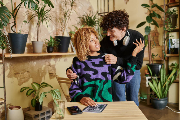 riccio giovane uomo abbracciando la sua ragazza afro-americana seduta vicino al menu sul tavolo del caffè vegan - Foto, immagini