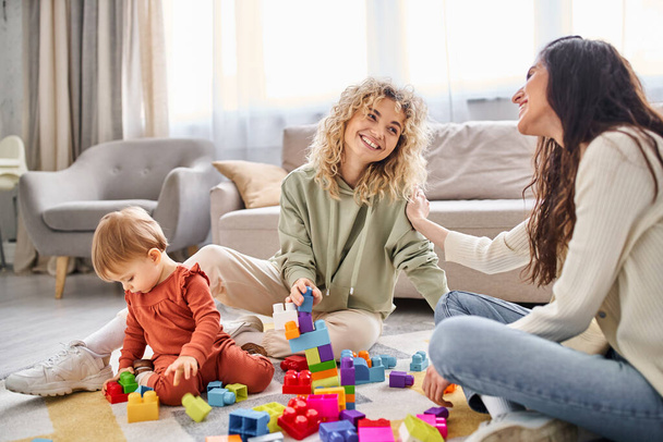 joyeux couple attentionné lgbt jouer avec leur petite fille avec des jouets sur le sol à la maison, concept de famille - Photo, image