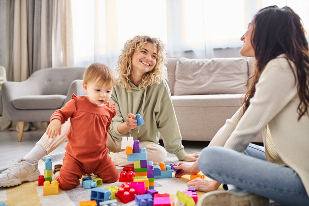 ενθουσιασμένοι λεσβιακό ζευγάρι παίζει με το κοριτσάκι τους με τα παιχνίδια στο πάτωμα στο σπίτι, οικογενειακή έννοια - Φωτογραφία, εικόνα
