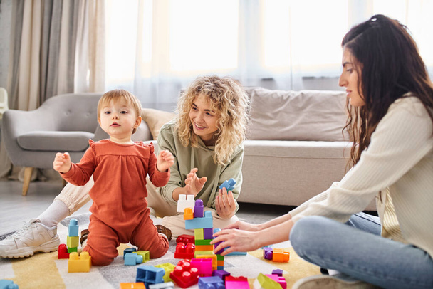 веселая лесбийская пара, играющая со своей малышкой с игрушками на полу дома, семейная концепция - Фото, изображение