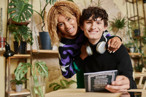 young affectionate african american woman embracing her curly boyfriend near menu in vegan cafe - Photo, Image