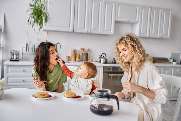 alegre atractivo lgbt pareja teniendo delicioso desayuno con su bebé niña, concepto de familia - Foto, Imagen