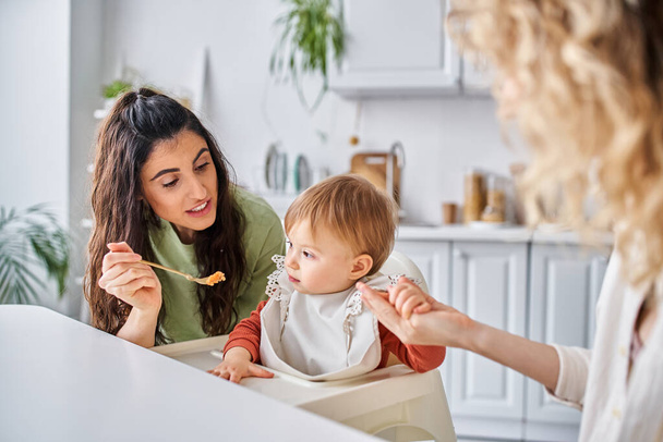 focus on jolly brunette woman with small daughter having breakfast next to blurred partner, family - Photo, Image