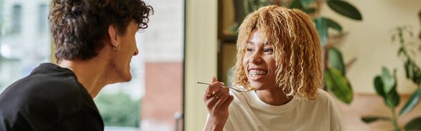 щаслива афроамериканка з брекетами їсть салат біля розмитого хлопця у веганському кафе, банер - Фото, зображення