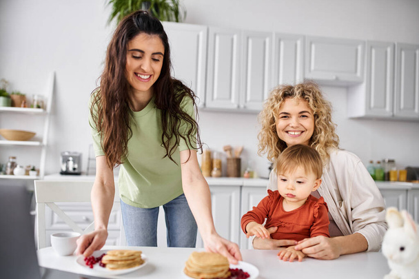 attractive joyful lesbian couple having pancakes on breakfast with their baby girl, family concept - Photo, Image