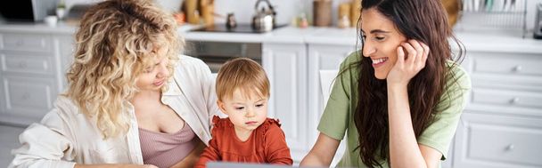 Ευτυχισμένο ζευγάρι Igbt βλέποντας ταινίες με την κόρη τους στο φορητό υπολογιστή στην κουζίνα, σύγχρονη ανατροφή των παιδιών - Φωτογραφία, εικόνα