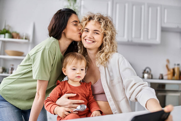 jolly lgbt couple spending time with their daughter with spoons in hand and holding phone, family - Photo, Image