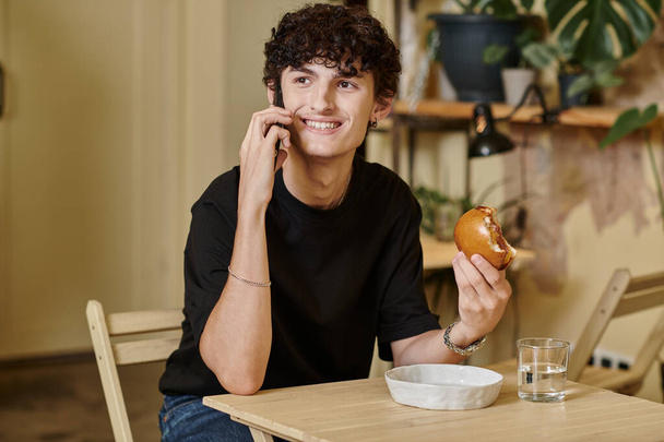 szczęśliwy i kręcone młody człowiek gospodarstwa roślin tofu burger i rozmowy na smartfonie w wegańskiej kawiarni - Zdjęcie, obraz