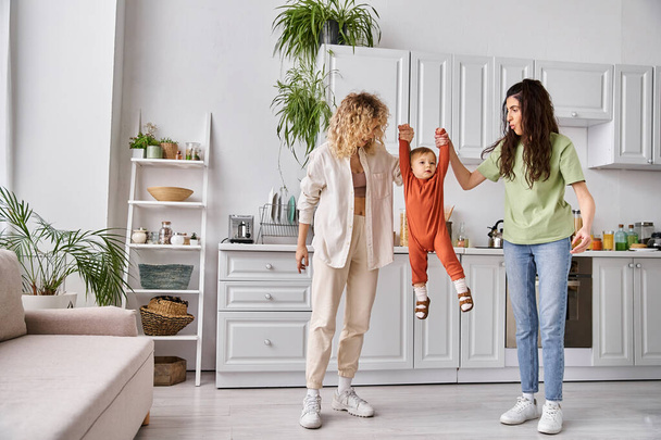 attractive merry lesbian couple playing actively with their toddler daughter, modern parenting - Photo, Image