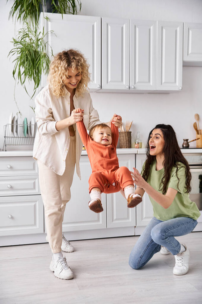 attractive cheerful lesbian couple playing actively with their toddler daughter, modern parenting - Photo, Image