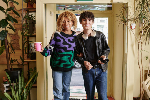позитивна різноманітна пара в повсякденному вбранні, дивлячись на камеру, стоячи разом у веганському кафе - Фото, зображення