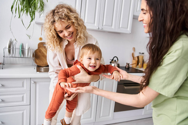attractive cheerful lgbt couple playing with their pretty little daughter on kitchen, family concept - Photo, Image