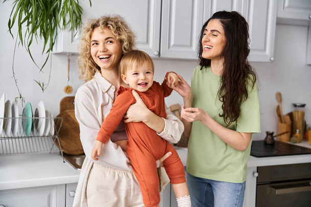 charming joyful lgbt couple playing with their pretty little daughter on kitchen, family concept - Photo, Image