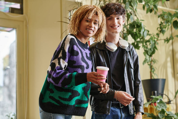 couple joyeux et diversifié en tenue décontractée regardant la caméra tout en se tenant ensemble dans un café végétalien - Photo, image