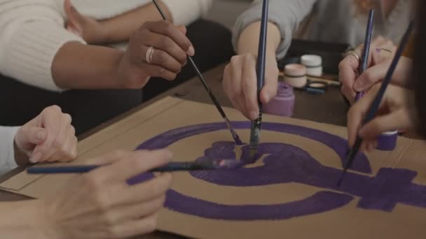 Обрезанный снимок неузнаваемой группы женщин с помощью кистей и фиолетовых красок при рисовании феминистского символа на картонной бумаге - Кадры, видео