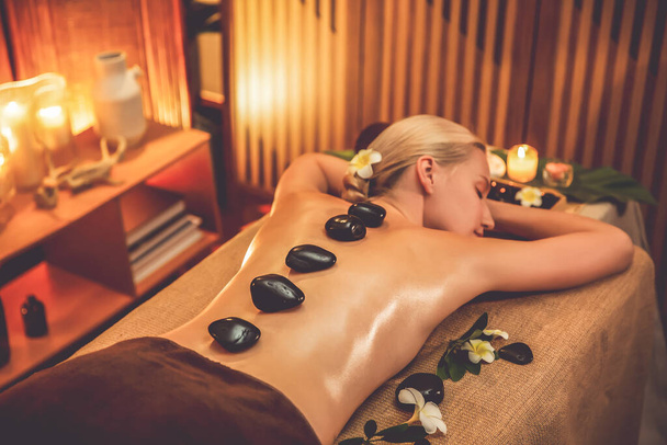 Hot-Stone-Massage im Wellness-Salon im Luxus-Resort mit warmem Kerzenlicht, glückselige Kundin genießt Wellness-Basaltsteinmassage gleiten mit wohltuender Wärme über den Körper. Ruhige Lage - Foto, Bild