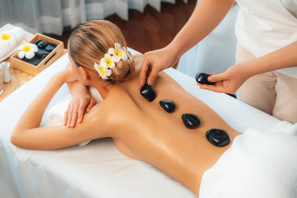 Hot-Stone-Massage im Wellness-Salon im Luxus-Resort mit Tageslicht Gelassenheit Ambiente, glückselige Kundin genießen Wellness-Basaltstein-Massage gleiten über den Körper mit wohltuender Wärme. Ruhige Lage - Foto, Bild