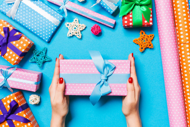 Top view of female hands holding a Christmas present on festive blue background. Holiday decorations and wrapping paper. New Year holiday concept. - Photo, Image