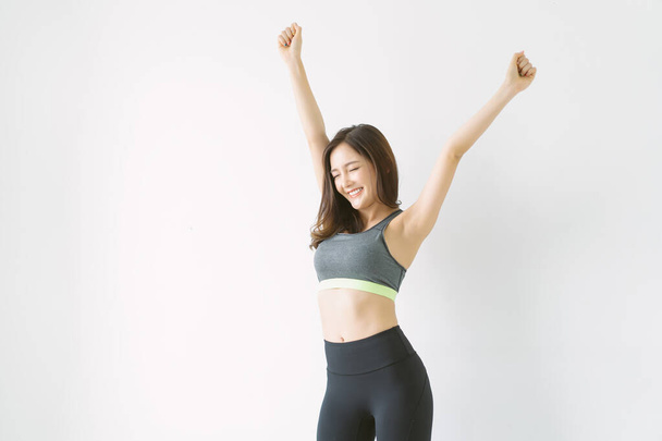 Красиве тіло струнка впевнена азіатська корейська в спортивному одязі позує підняти руки з очима, закритими на білому тлі стіни з копійкою для тексту. Спорт і здоровий спосіб життя - Фото, зображення