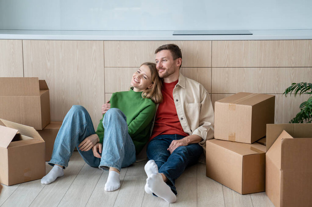 Mutlu çift erkek kadın yeni bir dairede yaşamayı hayal ediyor. Evdeki mutfakta yerde oturuyor. Taşınmak, daireye taşınmak, aile ipoteği konsepti. Hayattan zevk alan eşler dinleniyor. - Fotoğraf, Görsel