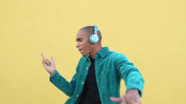 Mladý černošky muž poslech hudba píseň na bezdrátové modré sluchátka přes žlutou zeď  - Záběry, video