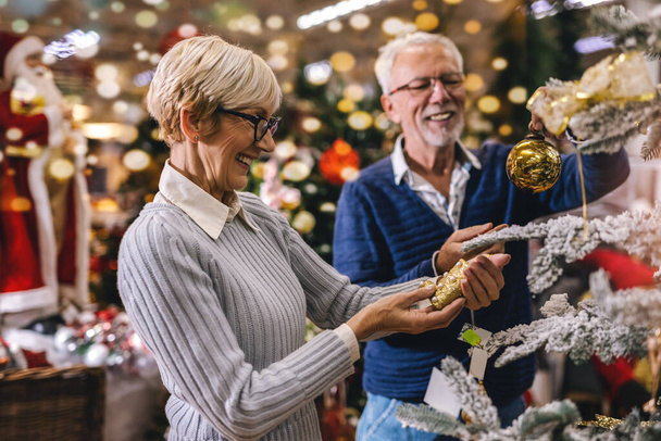 Az idősebb pár a karácsonyi piacon dekorációs játékokat és labdákat vesz. A karácsonyi és újévi vásárlás koncepciója. - Fotó, kép