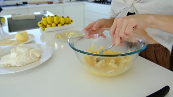 Een vrouw in de keuken maakt huiswerk. vrouw roert omelet met kaas op kom aan tafel. Binnenhuiskeuken. Ontbijtbereiding. - Video