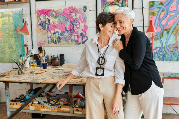 heureux et élégant artistes lesbiennes souriant avec les yeux fermés dans le studio d'art, relation harmonieuse - Photo, image