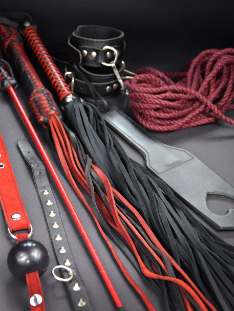 Leather flogger whip sex toys on a dark background stock photo images. Set of erotic toys for BDSM stock photo. Adult sex toy, flogger, ball gag, collar, rope, paddle, handcuffs images - Photo, Image