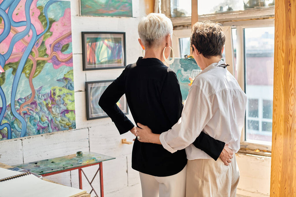 takaisin näkymä tyylikäs lesbo pari taiteilijoita syleilee ja seisoo modernin taiteen työpaja - Valokuva, kuva