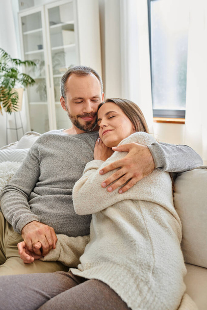 feliz pareja sin niños con los ojos cerrados abrazando en acogedor sofá en la sala de estar, estilo de vida tranquilo - Foto, Imagen